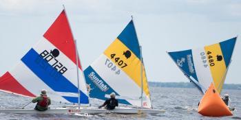 three boaters on boats with colorful sails in the river