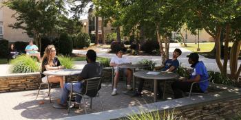 Students sitting and talking at outside tables in courtyard