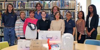 Students and staff pose in the library with two sets of virtual reality equipment and accessories.
