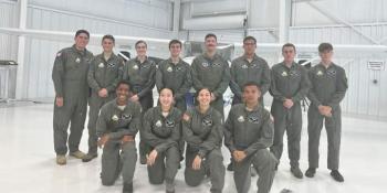 Twelve students in flight school camp pose in the hangar wearing flight suits