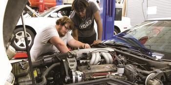 Two male students in the Automotive program work on a car