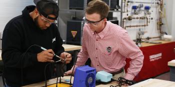 Male student works on engineering project while observed by male instructor