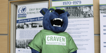 Blaze the panther blue and green mascot in front of college's 60th anniversary banners