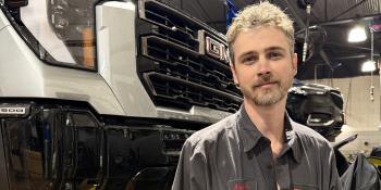 Automotive Systems Technology graduate Adam Heckman stands in front of a suspended car in the shop