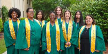 9 students stand in gray graduation robes