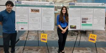 Two students stand with poster projects